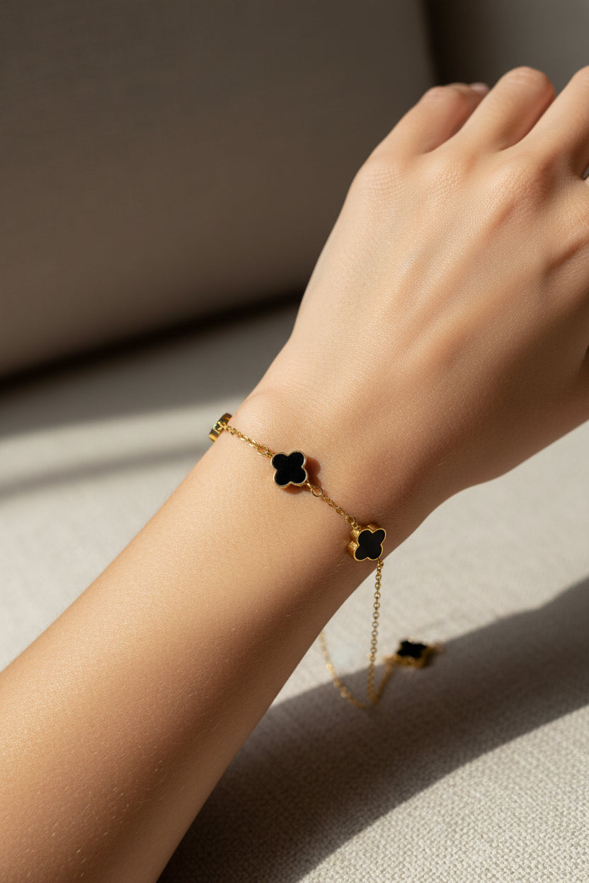 Gold bracelet with a black clover charm on a model's arm.
