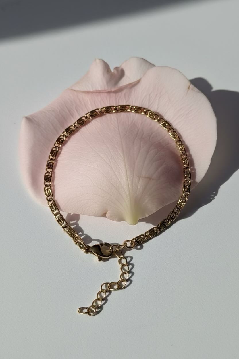 Gold bracelet on a pink rose petal with a white background
