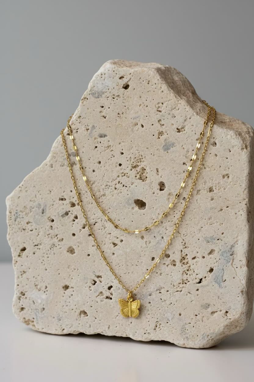Gold necklace set with a butterfly pendant on a textured stone surface