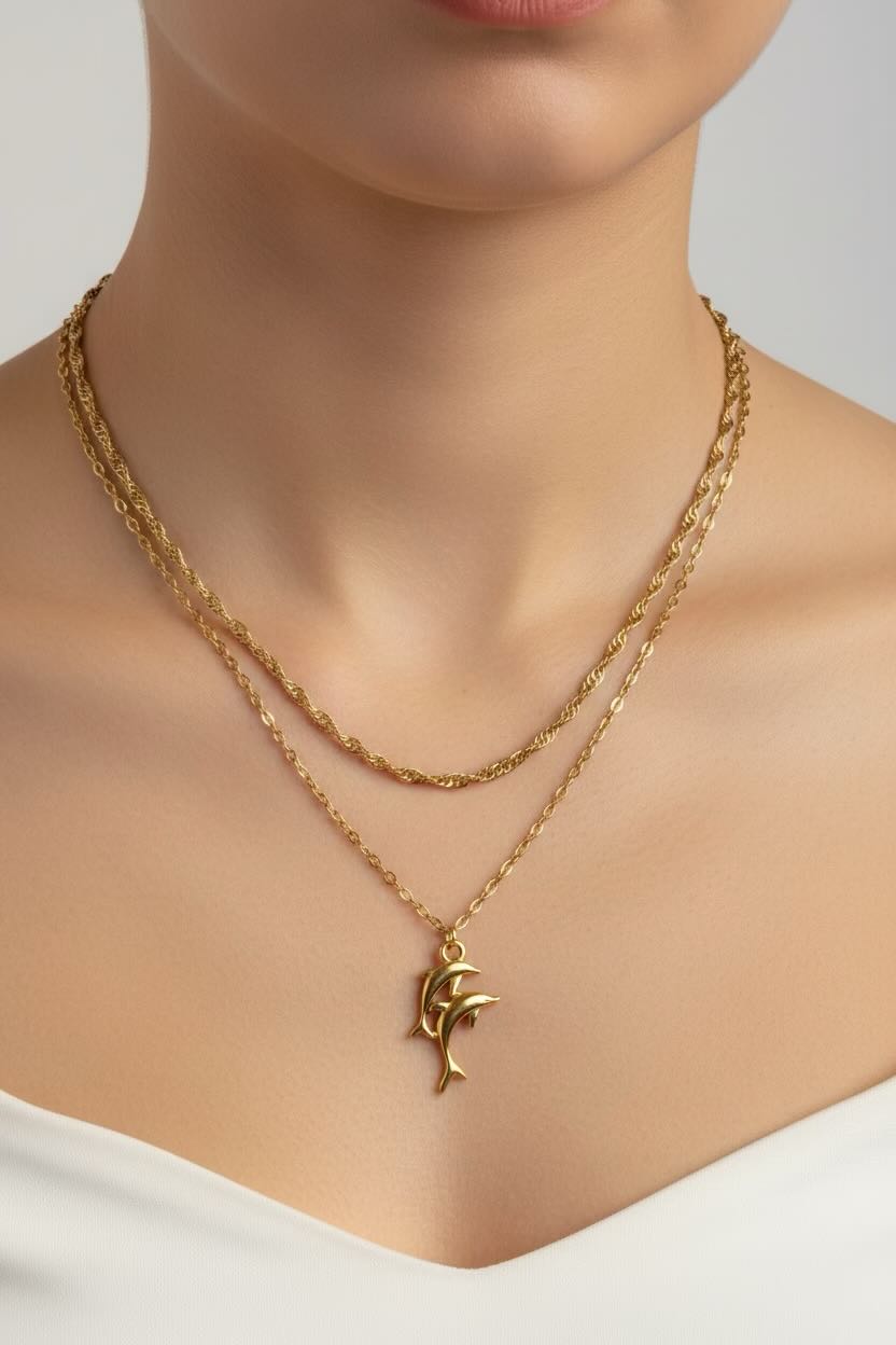 Gold necklace set with a double dolphin pendant on a mannequin