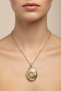 Gold oval flowered locket necklace with a decorative on a model's neck