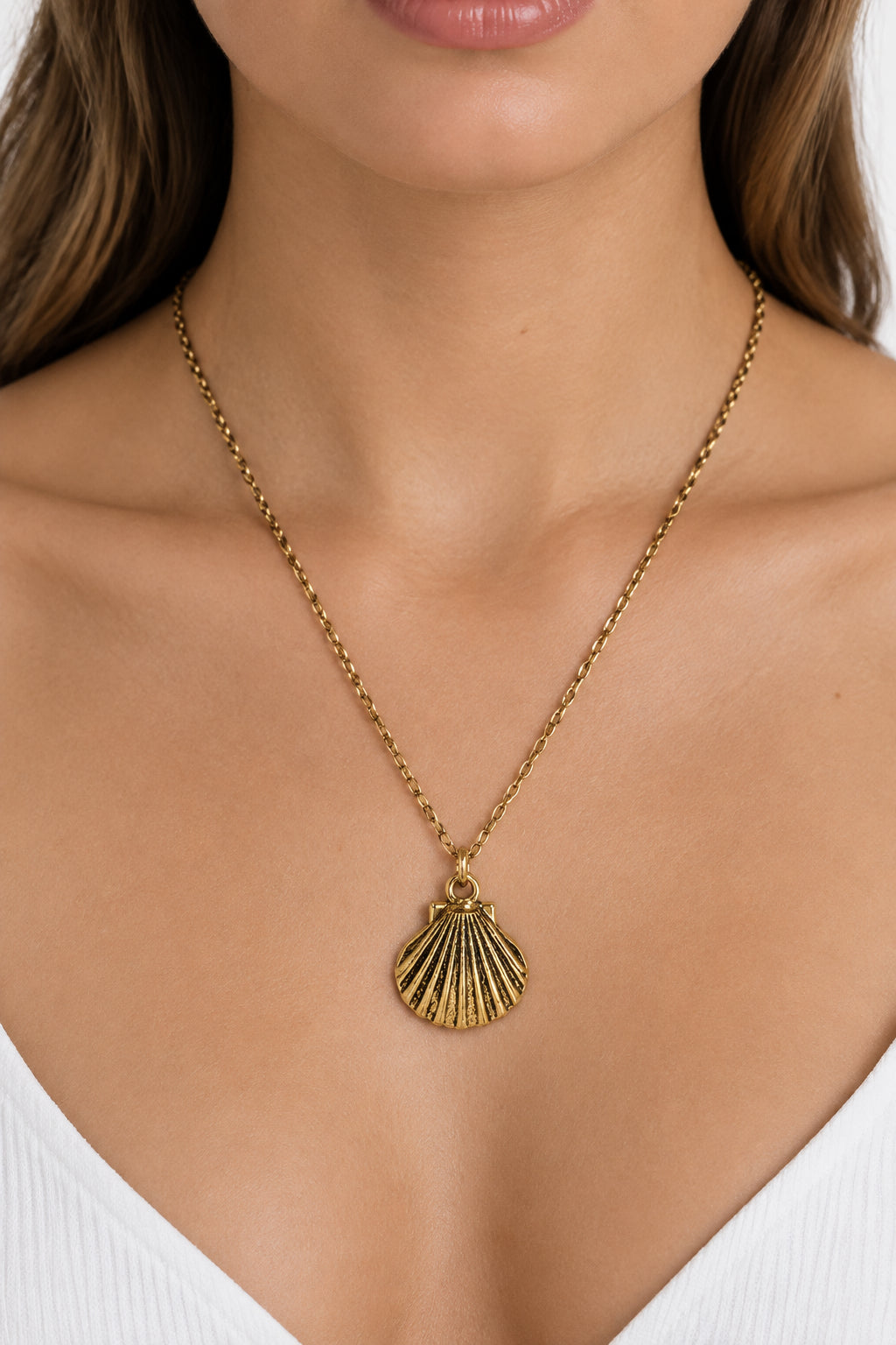 A gold-toned chain necklace with a textured scallop shell pendant, displayed on a white mannequin bust.