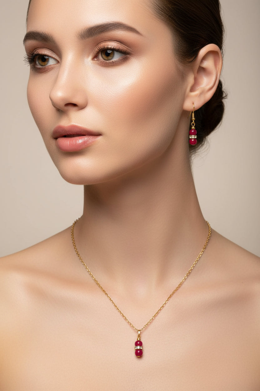 A gold-tone red pearl necklace and matching drop earrings on a model.