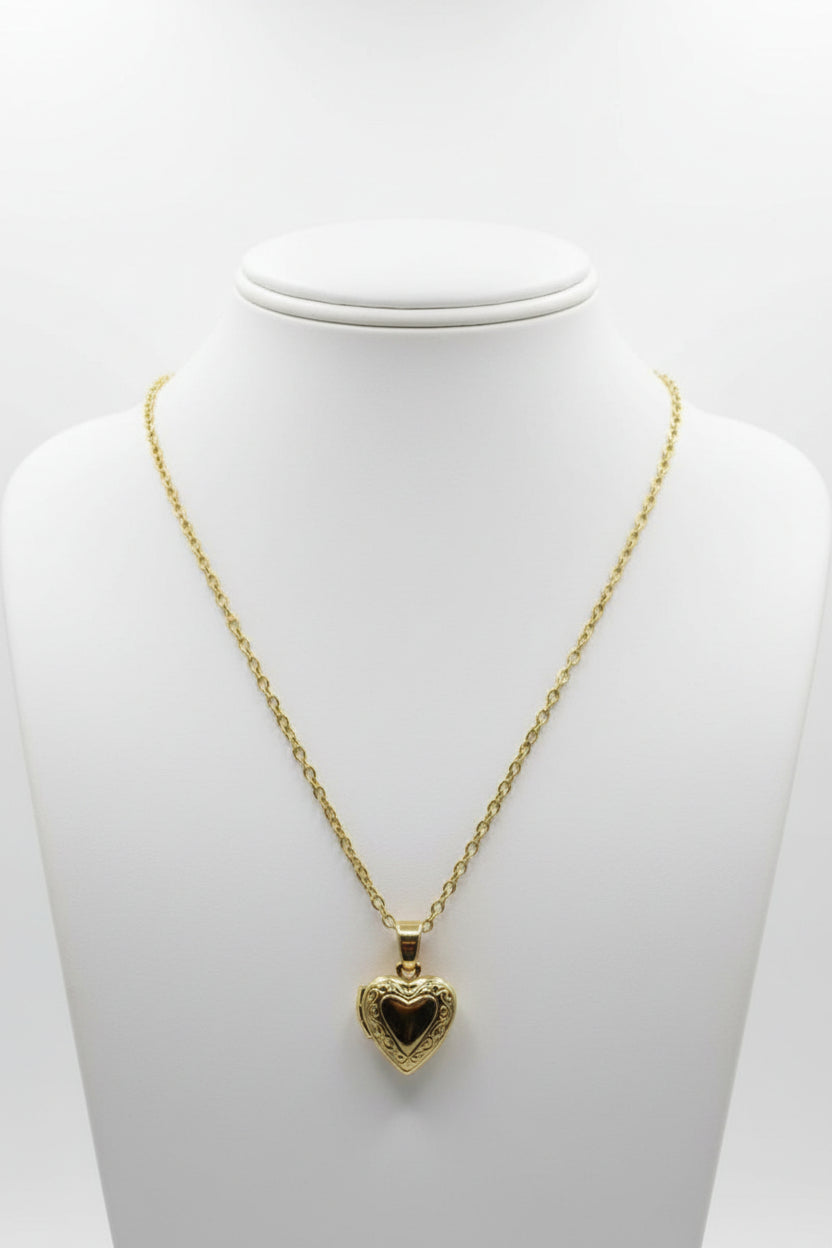 Gold brass heart-shaped locket on a stainless steel chain necklace on a mannequin with a plain background