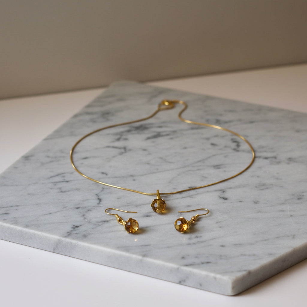Gold-tone necklace and matching drop earrings displayed on a white/grey marbled stone