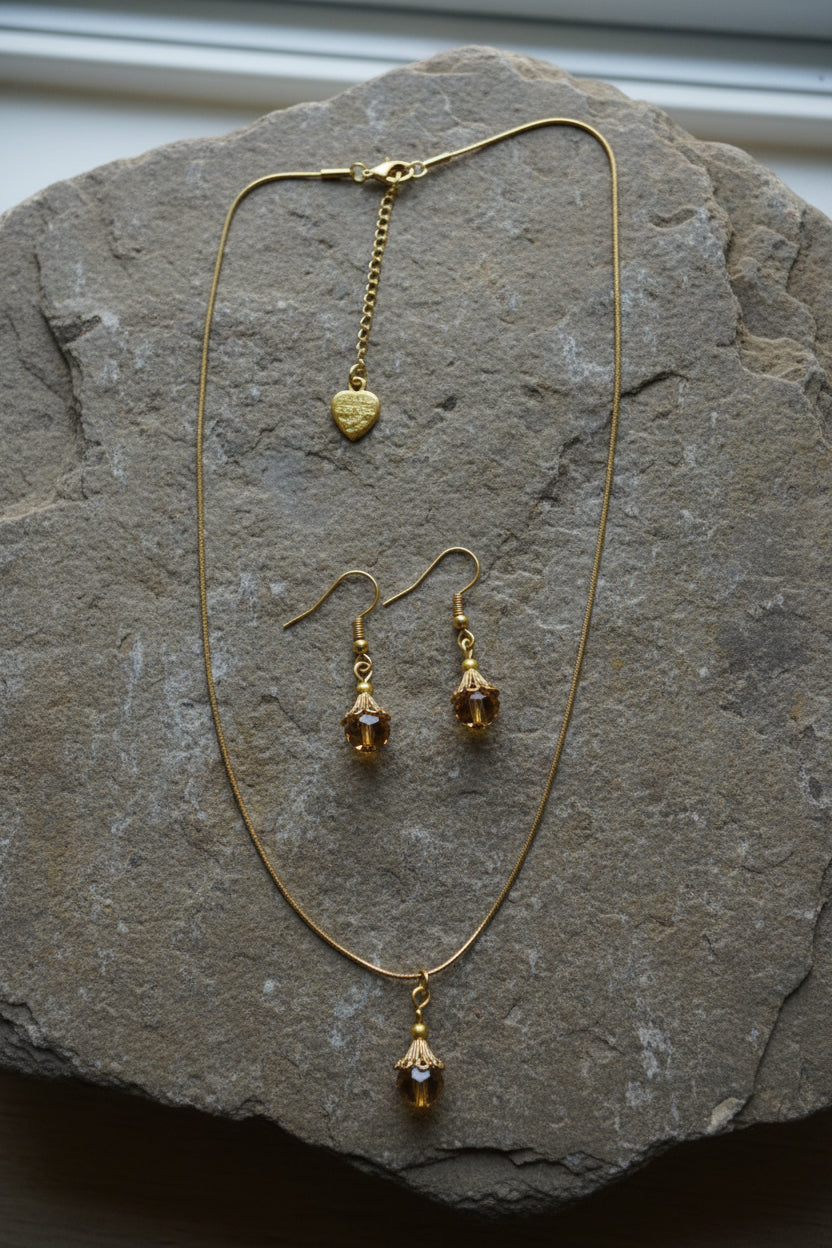 A gold-tone jewelry set featuring a delicate chain necklace with amber crystals and matching earrings on a large stone