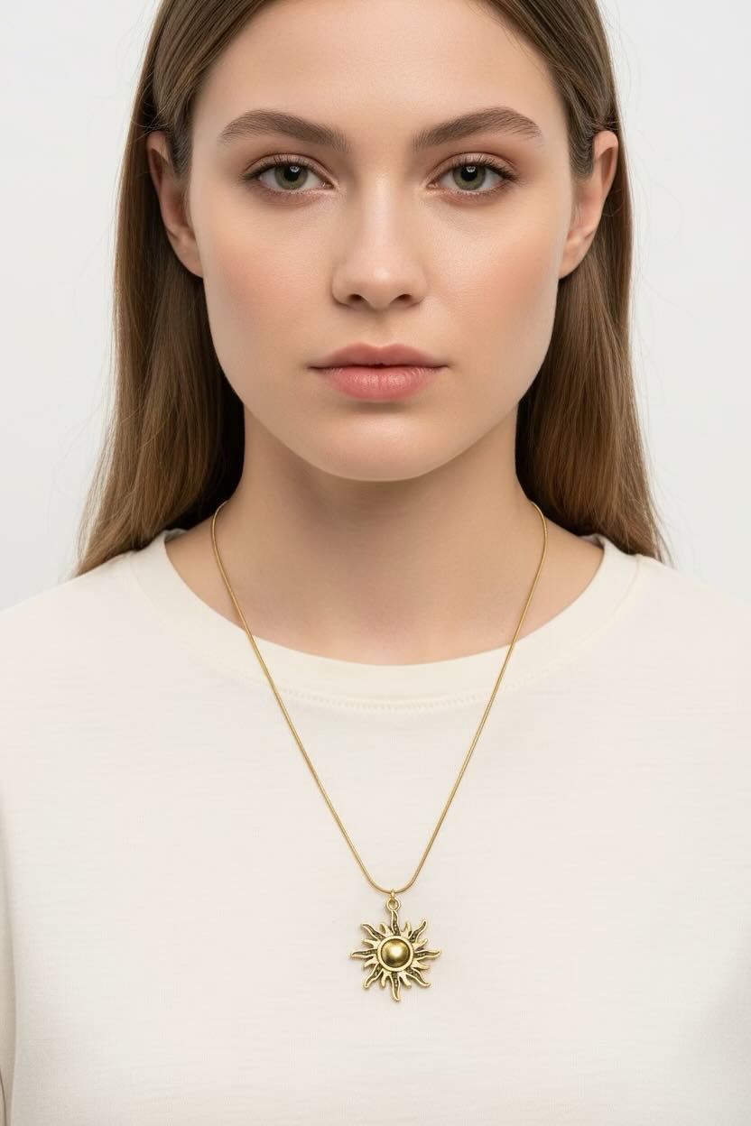 A woman wearing a delicate gold chain necklace with a sunburst pendant, shown against a plain light gray background.