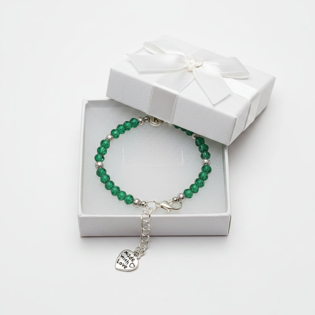 A beaded bracelet with green faceted beads, silver spacer beads, a round silver charm with a 'K' charm, displayed in a white gift box.