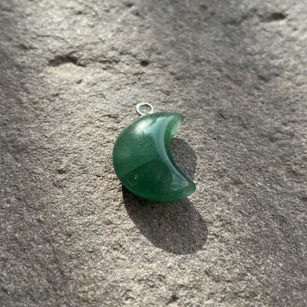 Green crescent moon-shaped pendant on a textured stone surface