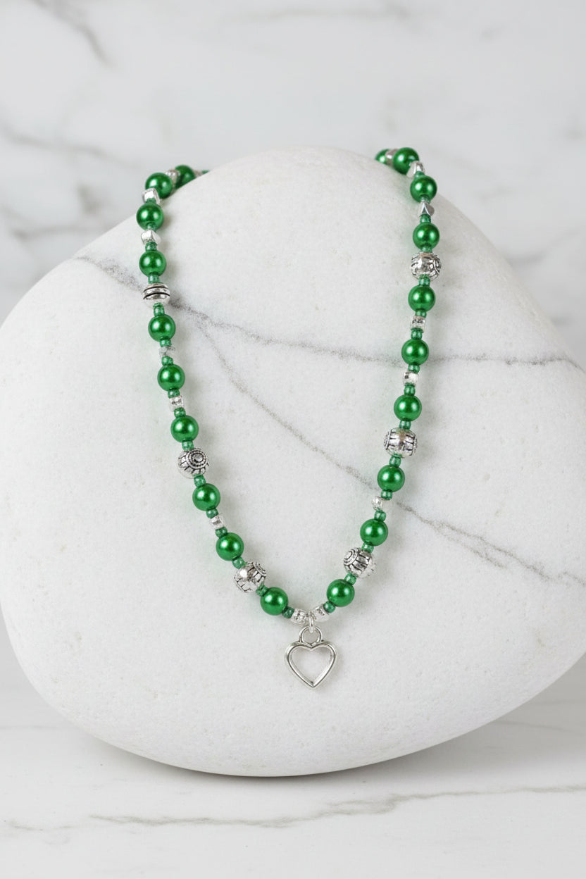Green beaded necklace with a heart pendant on a marble surface