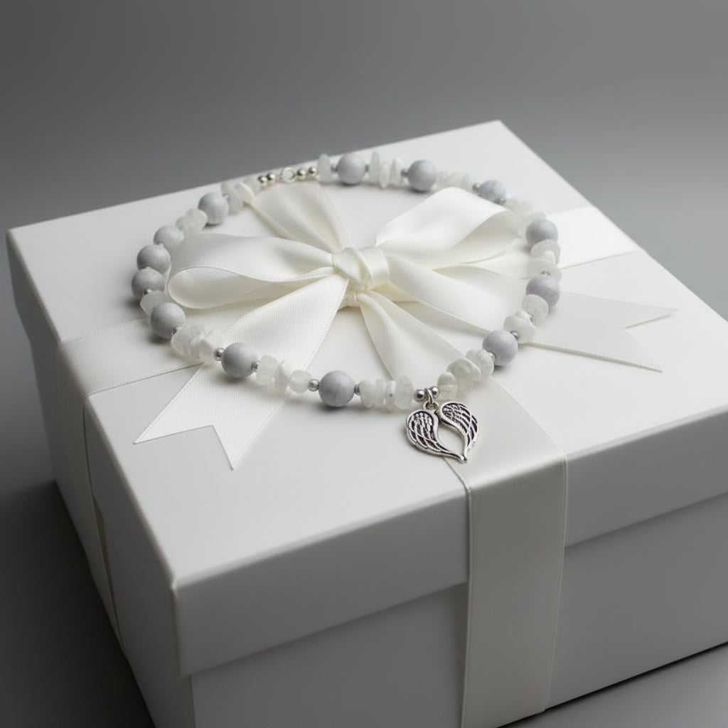 Necklace with gray and white beads and a angel wings pendant on a large gift box. 