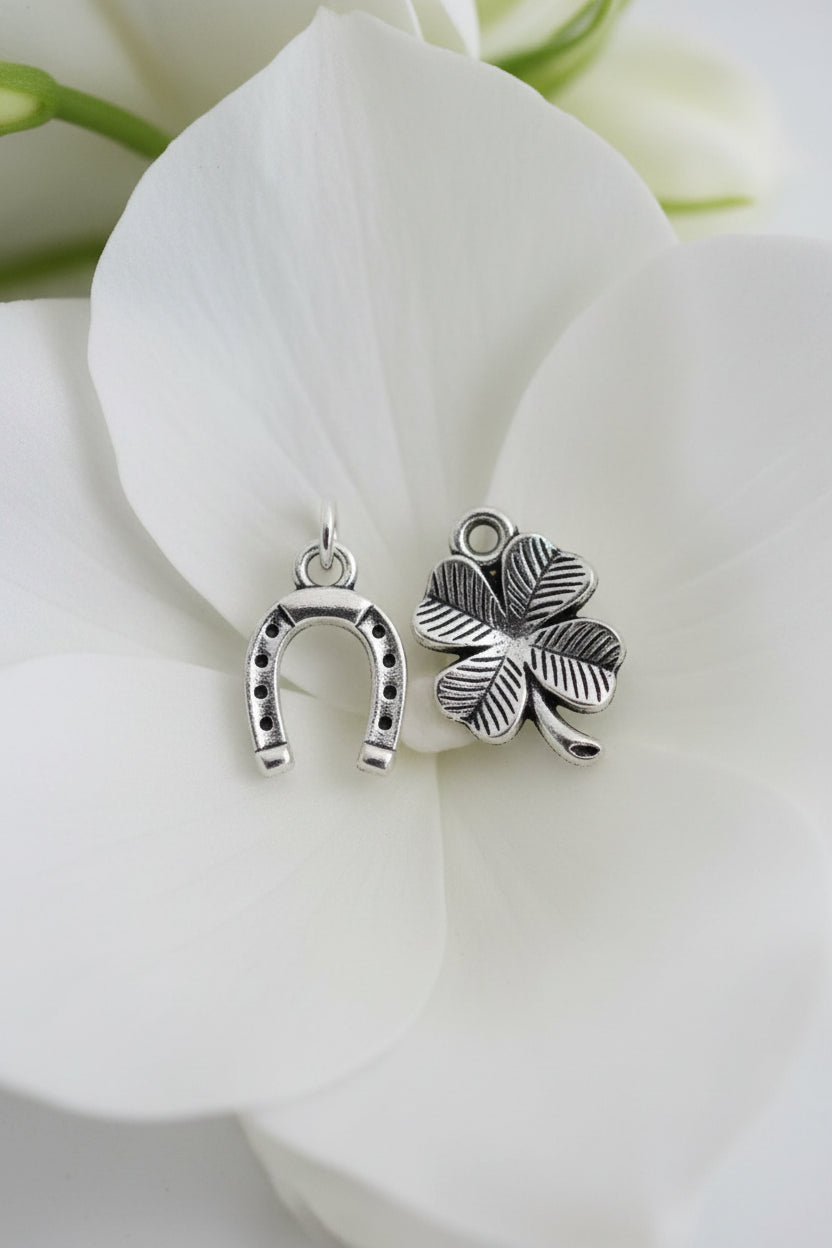 A silver-tone chain necklace with a charm featuring a four-leaf clover and a horseshoe, displayed on a light beige fabric background.