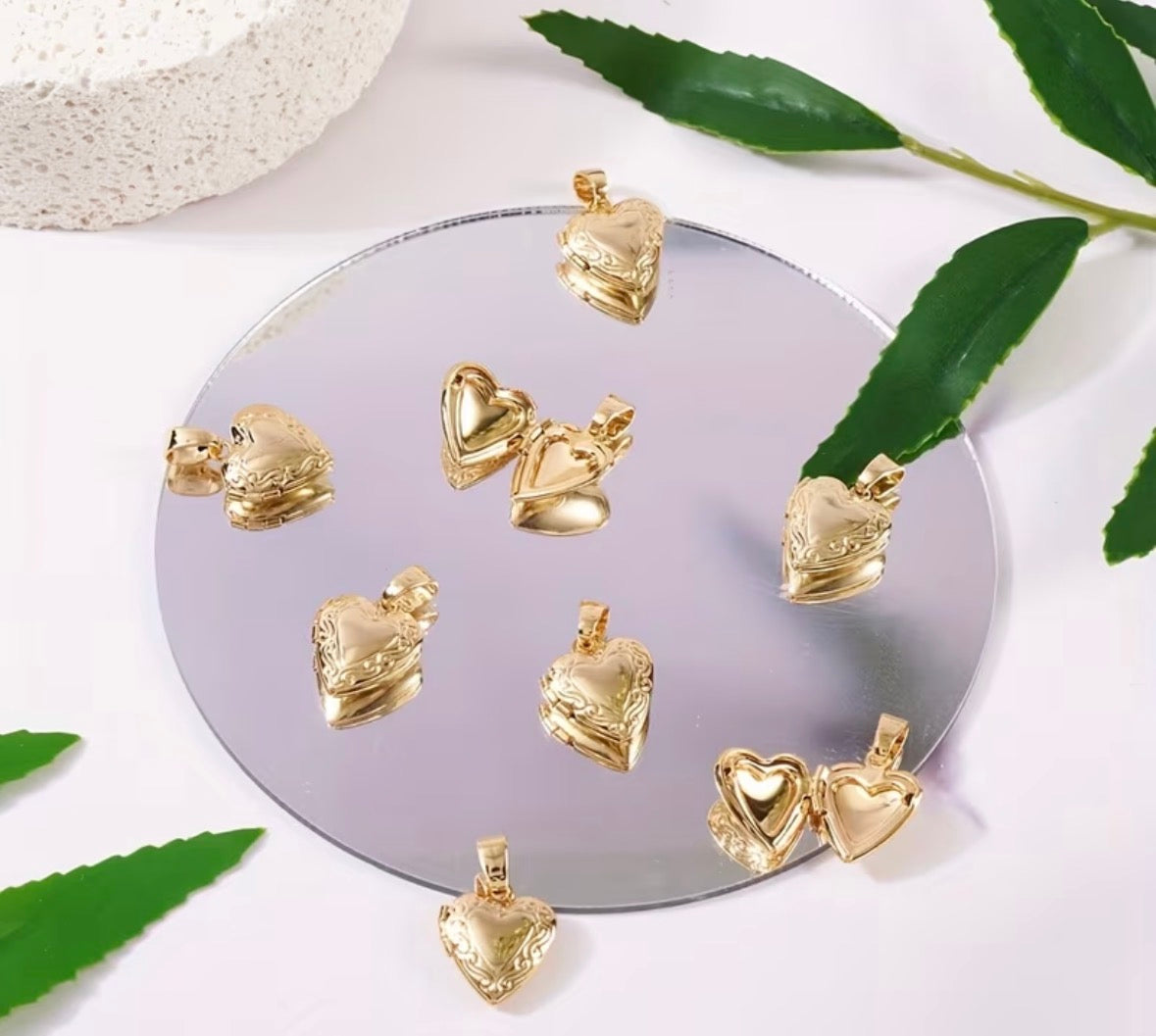 Gold heart-shaped pendants on a round mirror with green leaves around