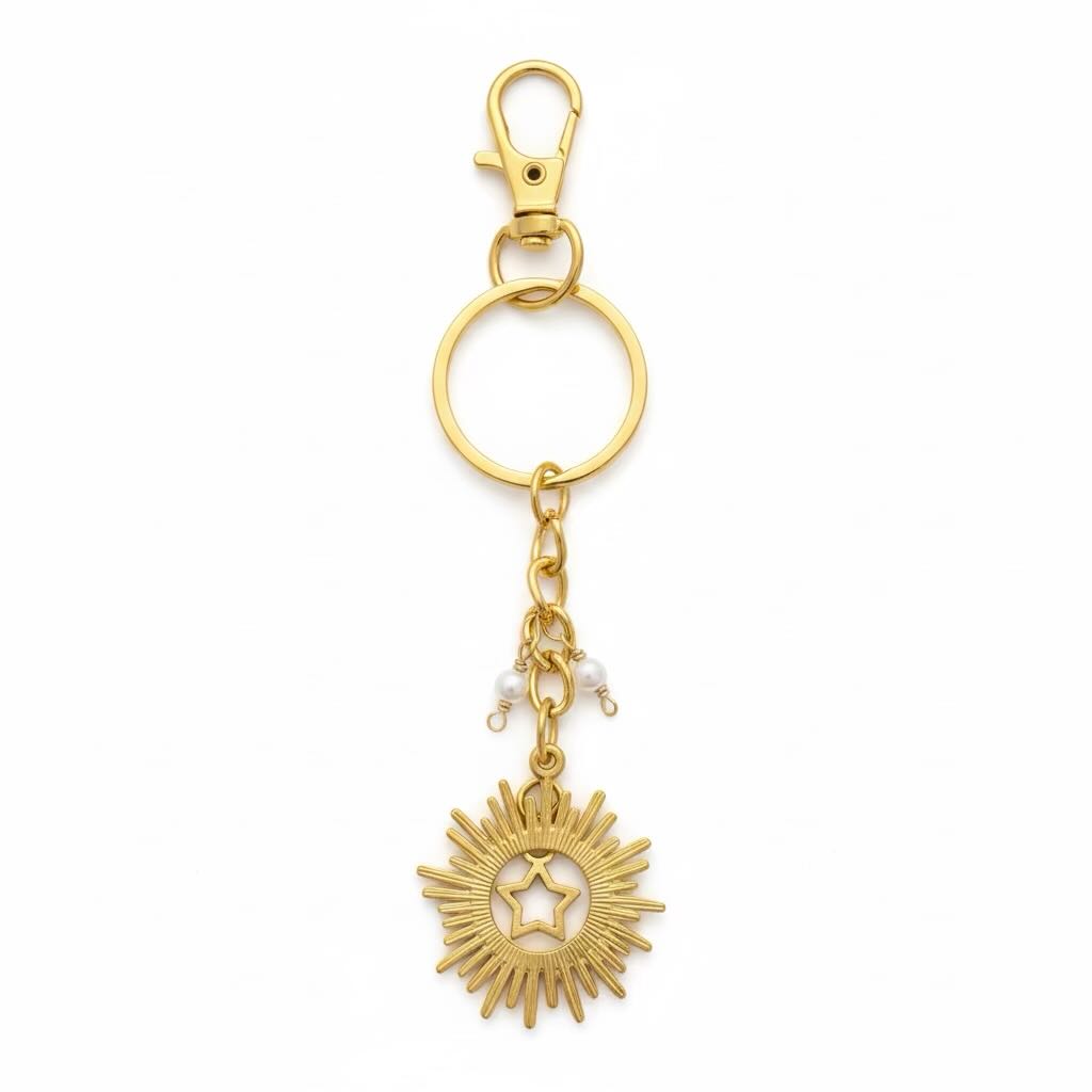 Gold-toned metal keyring with a lobster clasp, split key ring, small chain, pearl beads, and a sunburst star charm on a plain white background.