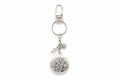 A silver-toned metal keyring featuring a round floral locket pendant, a small pink bead charm, and a silver flower charm, attached to a split ring and lobster clasp on a white background.