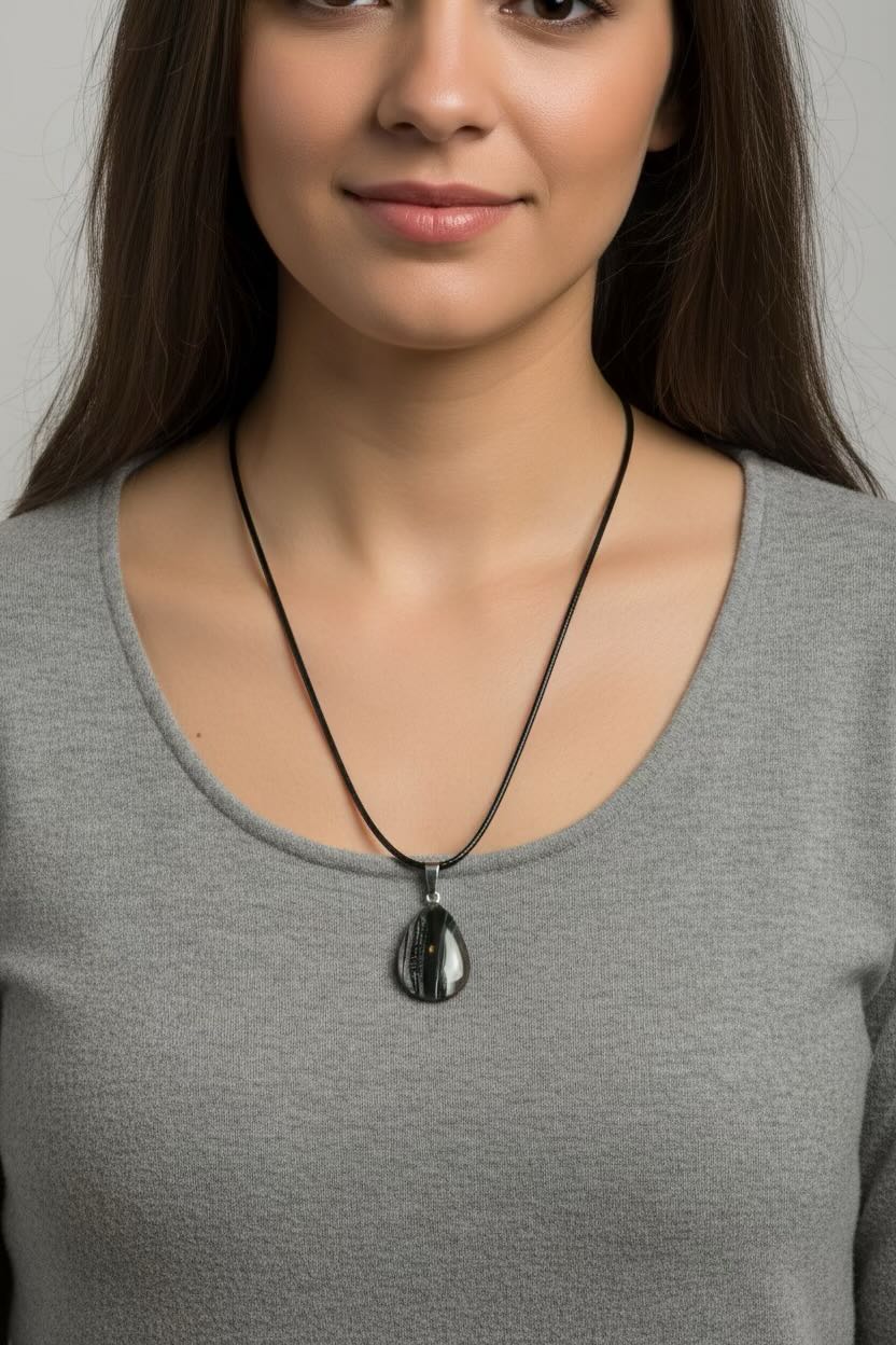 A woman wearing a black cord necklace with a black and clear teardrop-shaped pendant, shown from the chest up against a light gray background.
