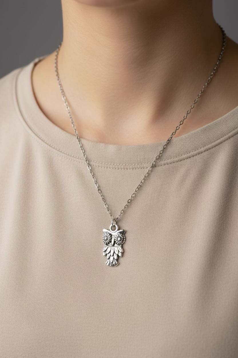 Silver owl pendant necklace on a person wearing a beige shirt