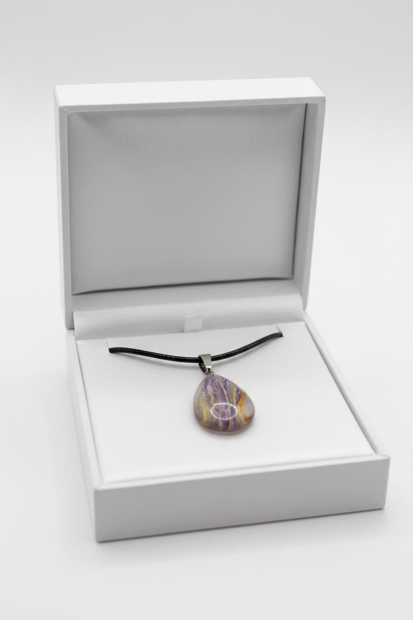 A teardrop-shaped pendant necklace with a purple and yellow marbled pattern, suspended on a black cord, presented inside an open white jewelry box.