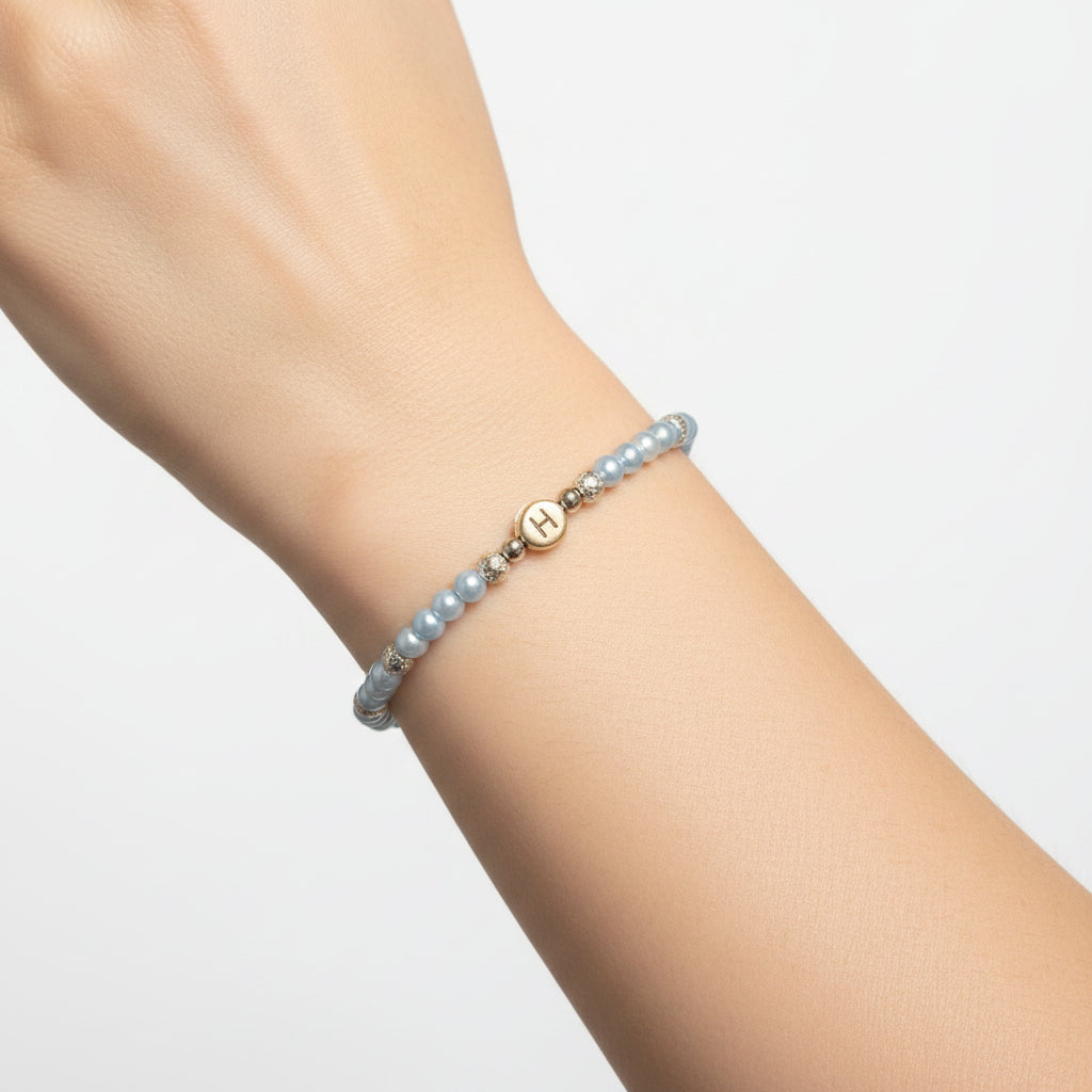 A beaded bracelet with light blue pearls, silver spacer beads, and a silver-toned charm engraved with the letter 'A', displayed on a white ceramic model's arm.