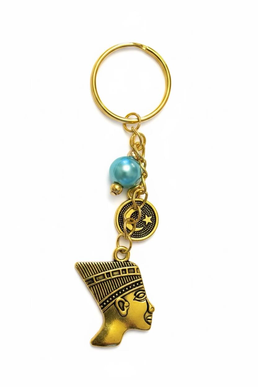 Gold-tone metal keyring featuring a profile of an ancient Egyptian pharaoh, a small round medallion charm, a light blue pearl bead, and a gold split ring, shown on a plain white background.