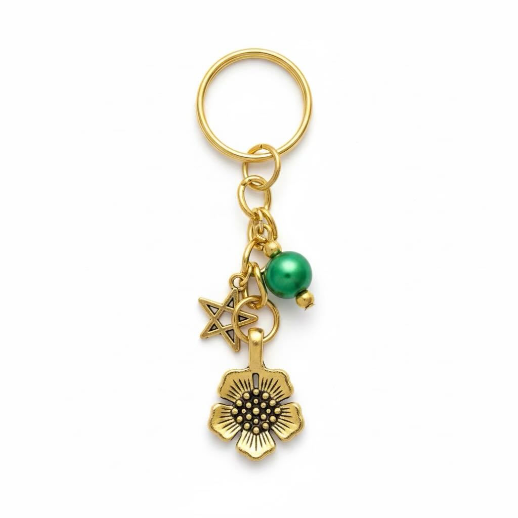 A gold-tone metal keyring featuring a circular key ring, a star charm, a flower charm, and a small green pearl accent, shown on a plain white background.