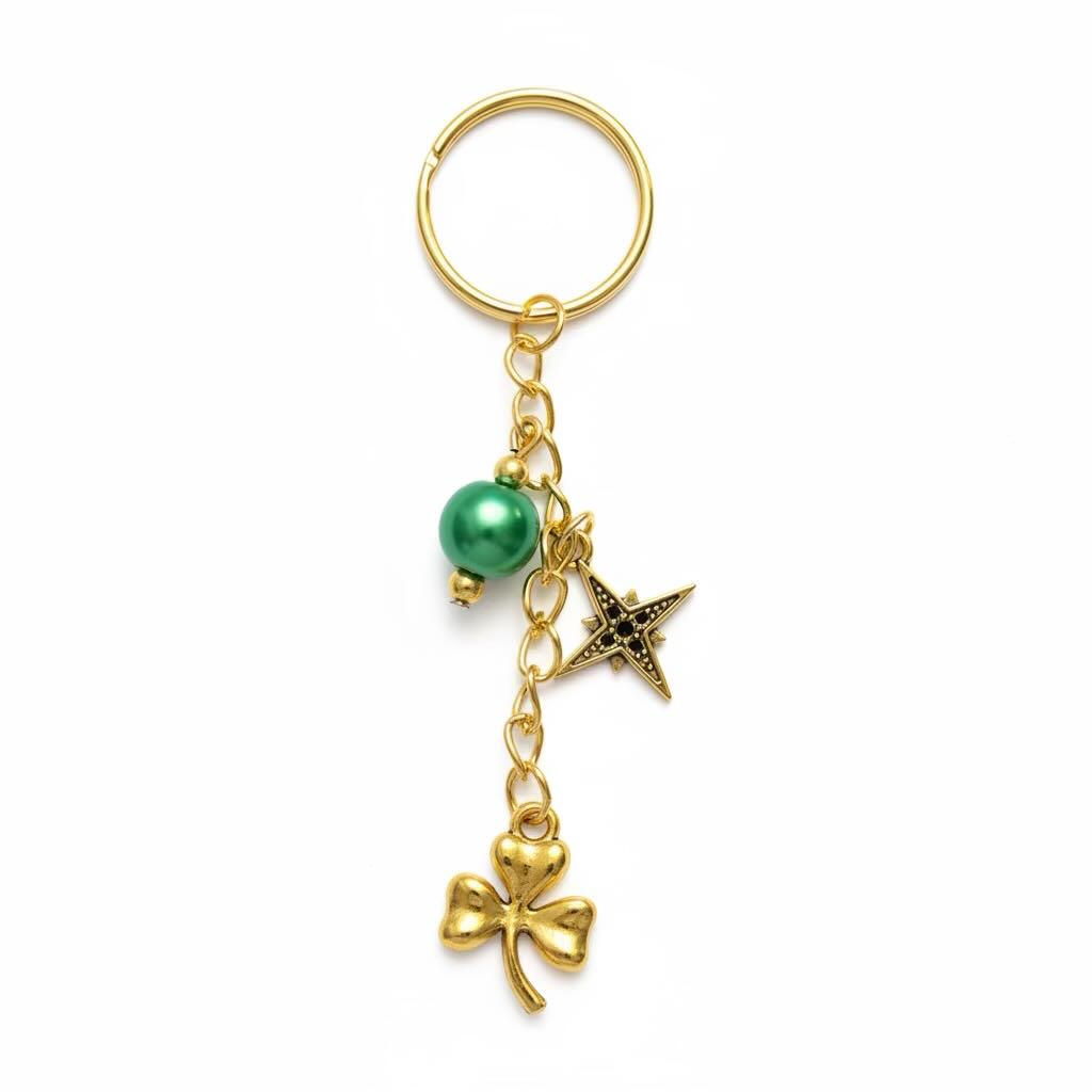 A gold-tone keyring featuring a St. Patrick's Day theme with a green pearl bead, a star charm, and a clover charm, attached to a split key ring on a white background.