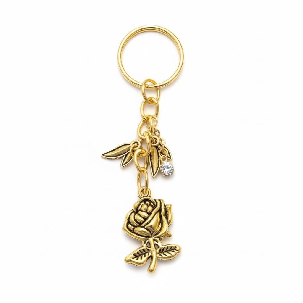 Gold-tone metal keyring featuring a rose and leaf charm, a small bird charm, and a clear rhinestone, attached to a split key ring on a white background.