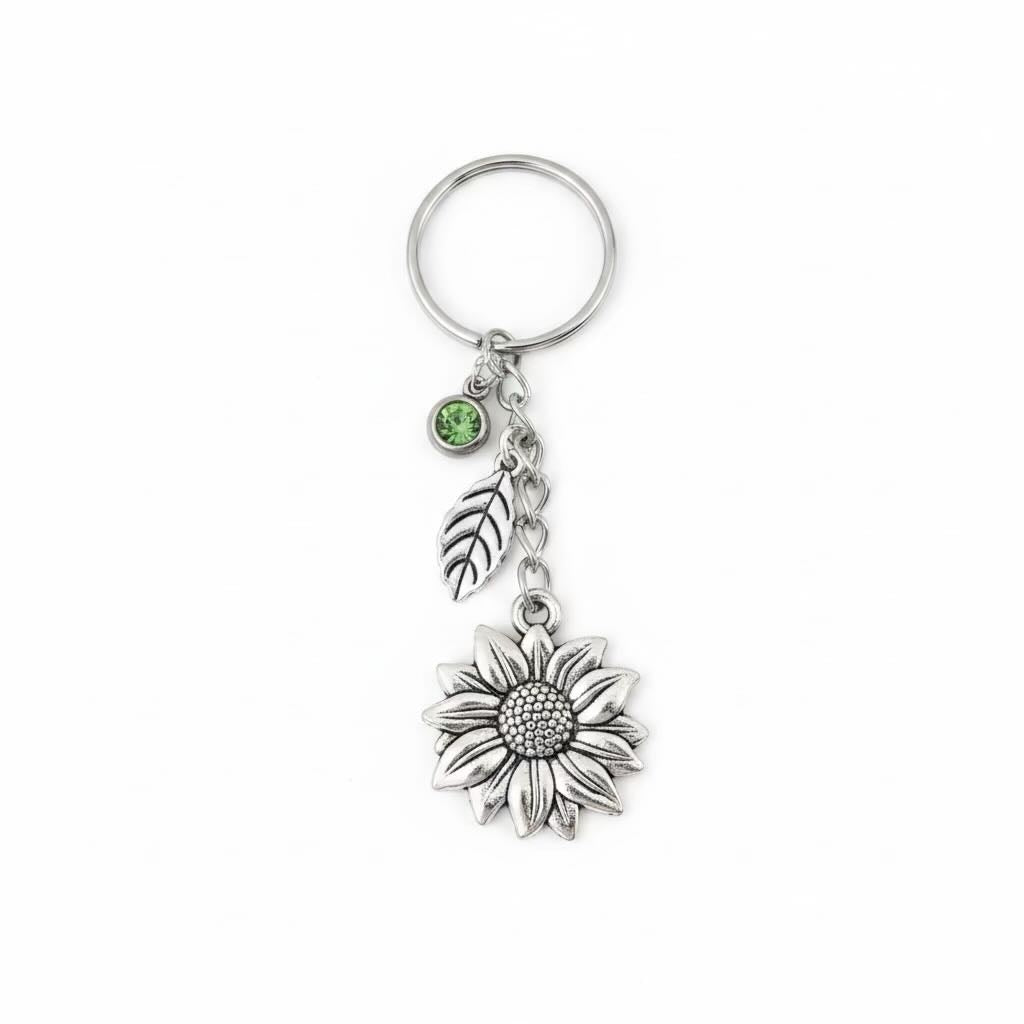 A silver-toned metal keyring/keyrings featuring a sunflower charm, a leaf charm, and a small round green gemstone accent, shown on a plain white background.