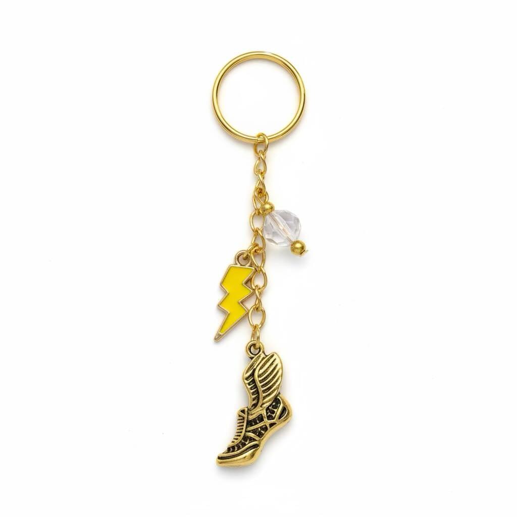 A gold-tone keyring featuring a split key ring, a small clear faceted bead, a yellow lightning bolt charm, and a winged sneaker charm, shown on a plain white background.
