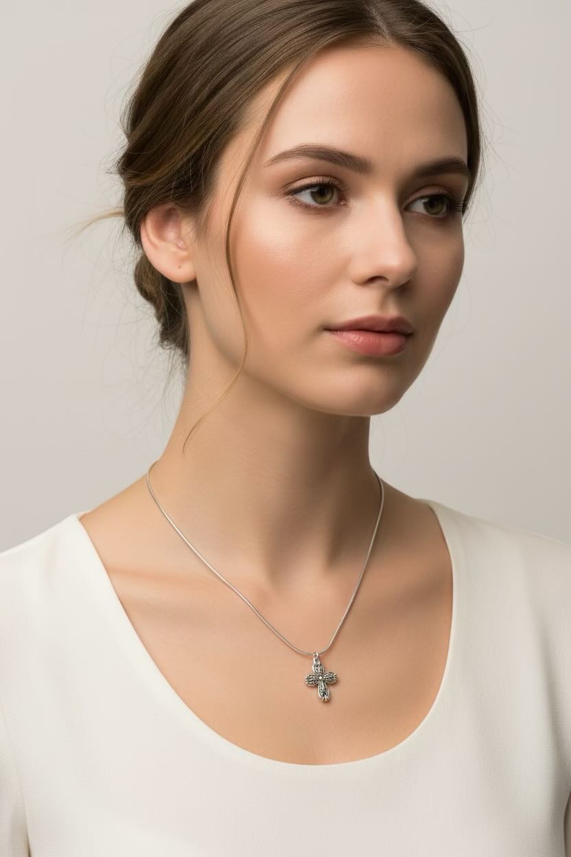 Woman wearing a necklace with a cross pendant against a plain background