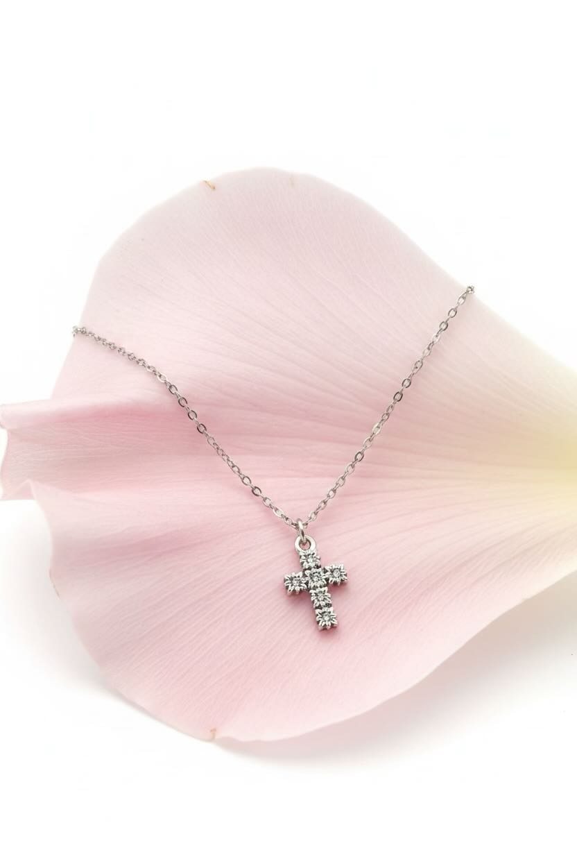 Silver cross necklace with clear stones on a pink petal background