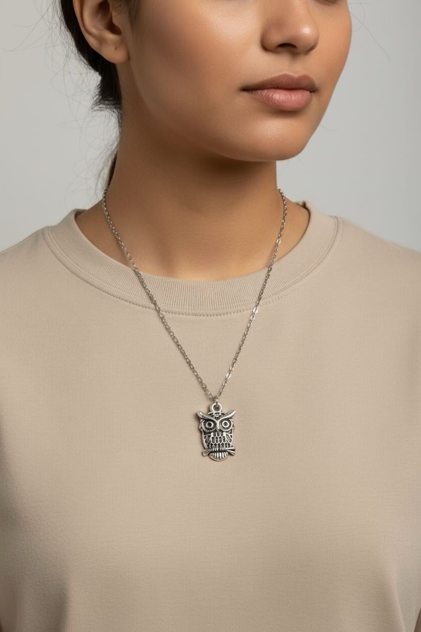 Person wearing a silver owl pendant necklace on a plain background