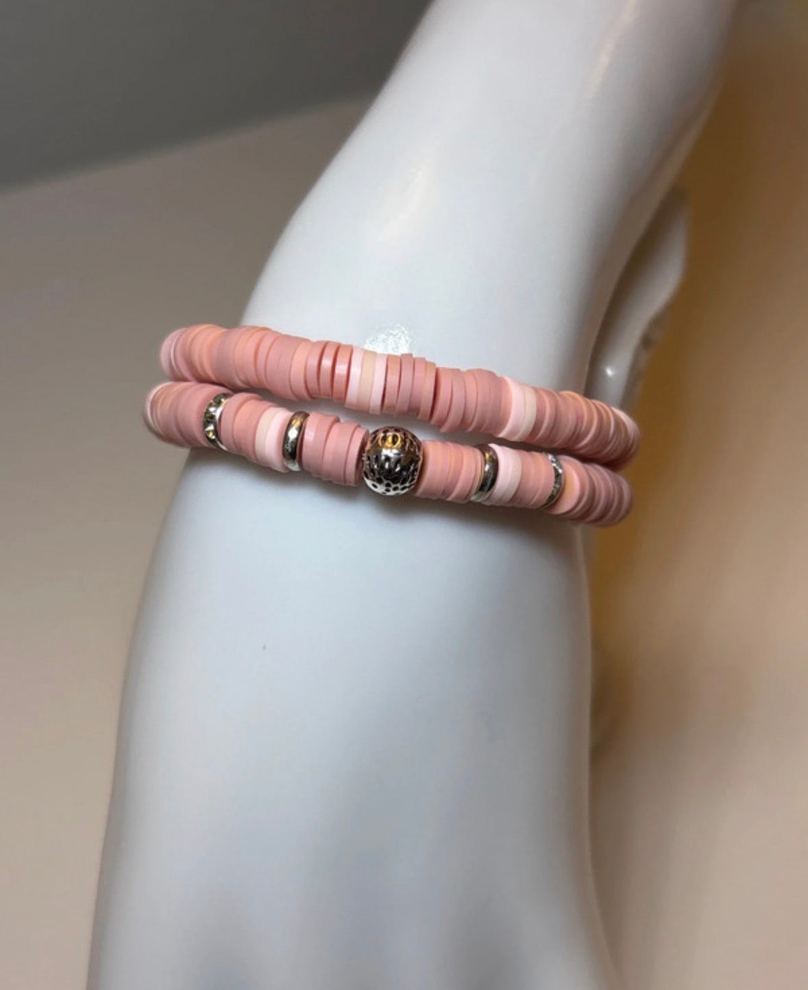 Pink beaded bracelet with a gold clasp on a mannequin arm against a neutral background