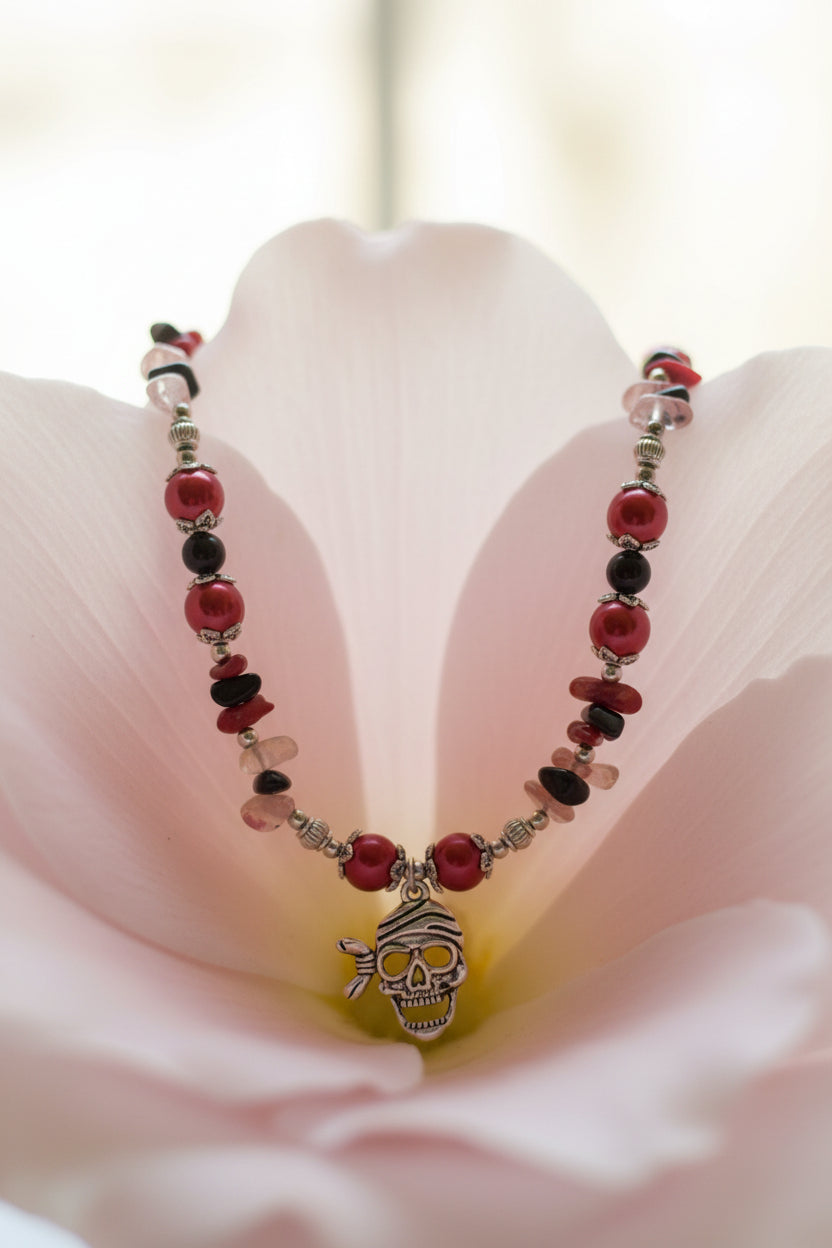 Necklace with red and black beads and a skull pendant on a pale pink petal