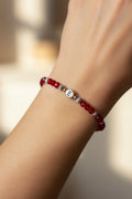 A red beaded bracelet with silver spacer beads and a central silver letter charm spelling 'E', displayed on a white model's arm
