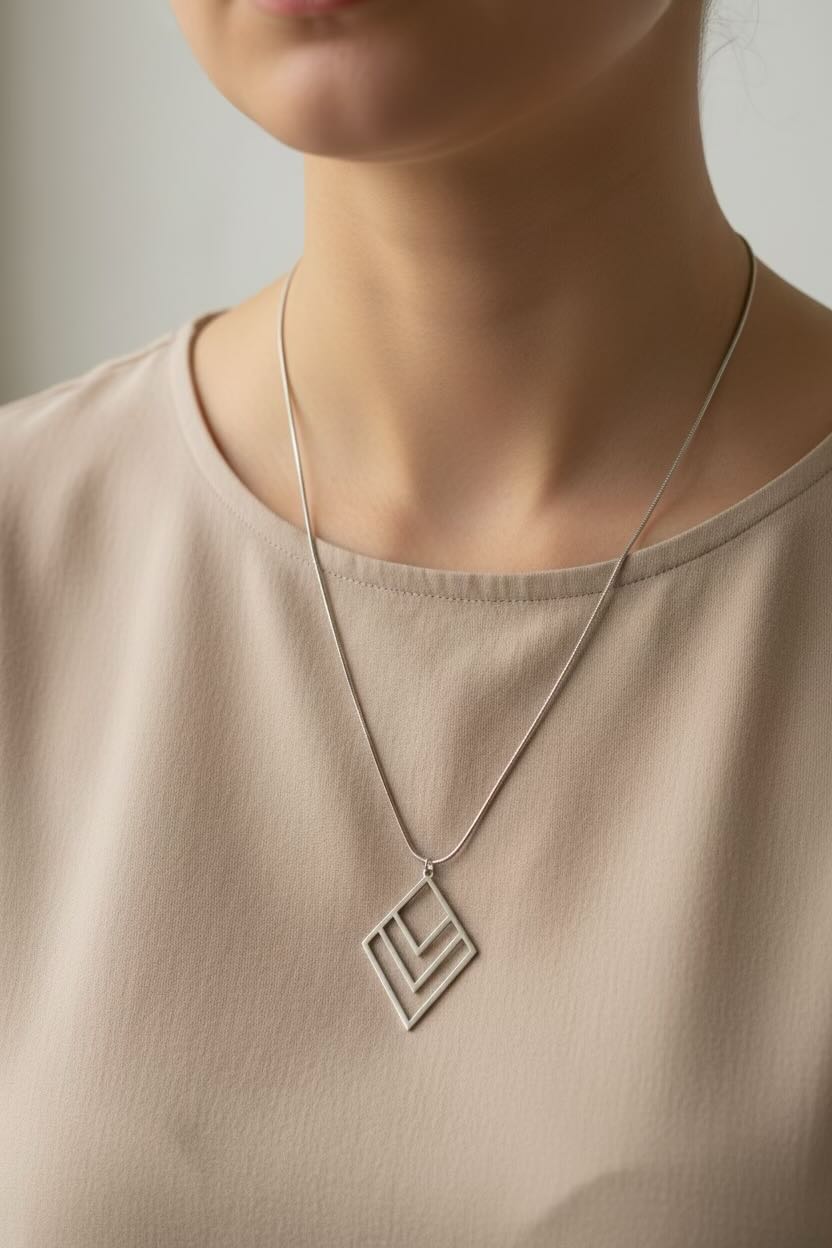 A close-up of a person wearing a delicate silver layered diamond chevron pendant necklace with a thin chain, paired with a beige top.