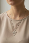 A close-up of a person wearing a delicate silver layered diamond chevron pendant necklace with a thin chain, paired with a beige top.