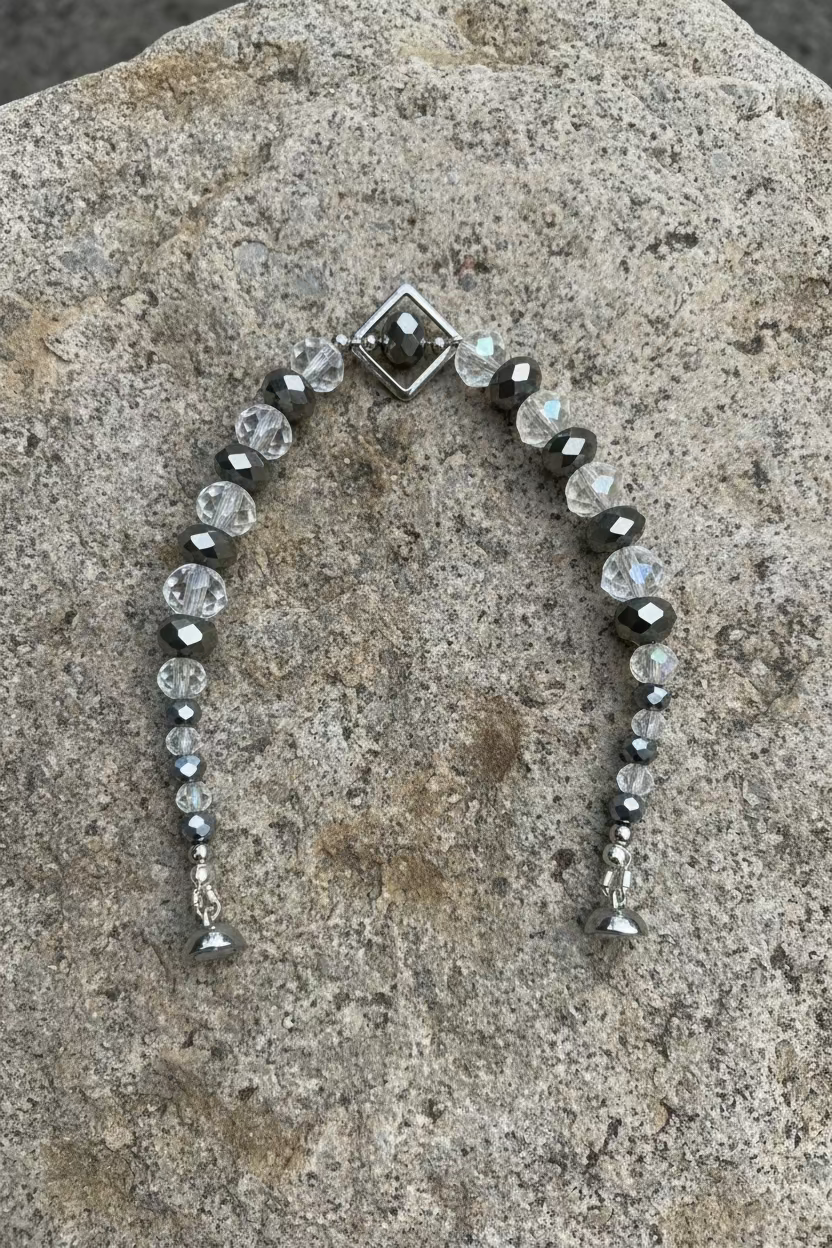 A beaded bracelet with faceted clear, gray, and iridescent beads, a silver-toned diamond-shaped frame with magnetic fastening, displayed on a grey stone.