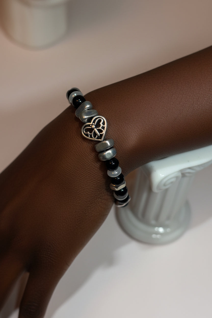 A beaded bracelet with black and silver metal stone beads and a central heart-shaped charm, displayed on a model.