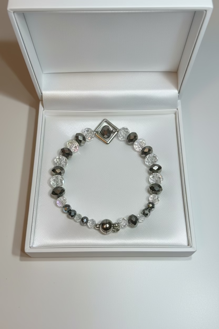 A beaded stretch bracelet featuring faceted clear, smoky gray, and iridescent beads, with a silver-toned metal magnetic fastening, displayed in a white gift box.