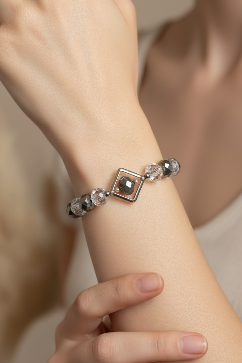 A beaded bracelet with faceted black and iridescent beads, featuring a central diamond silver-toned metal charm, displayed on a model's hand.