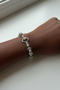 A beaded bracelet with faceted clear, smoky gray, and iridescent beads, accented by small silver-toned beads and a diamond silver frame, shown on a model's wrist.