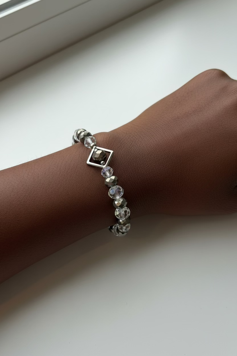 A beaded bracelet with faceted clear, smoky gray, and iridescent beads, accented by small silver-toned beads and a diamond silver frame, shown on a model's wrist.