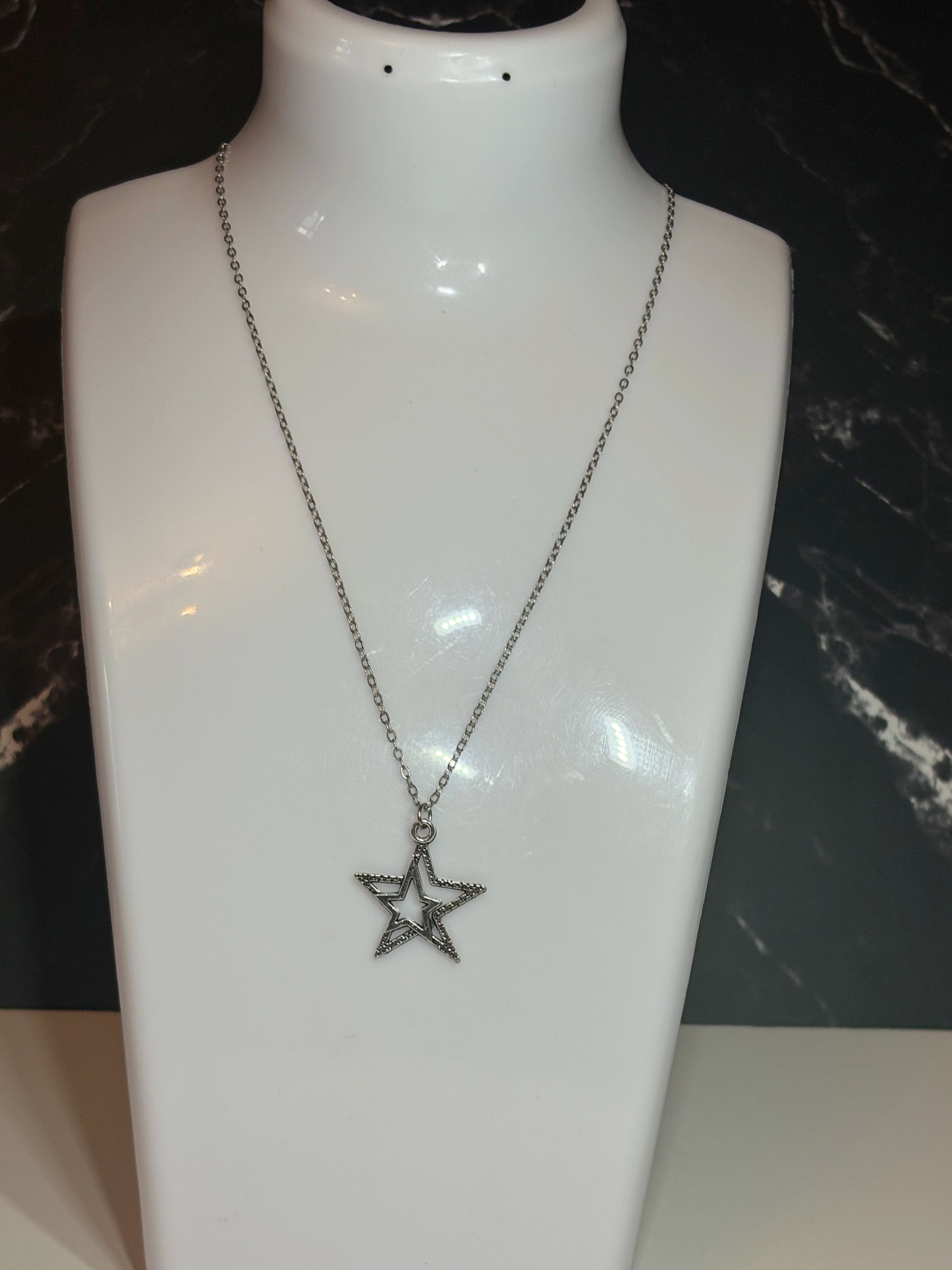 A silver-toned star pendant necklace displayed on a glossy white jewelry bust against a dark marbled background.