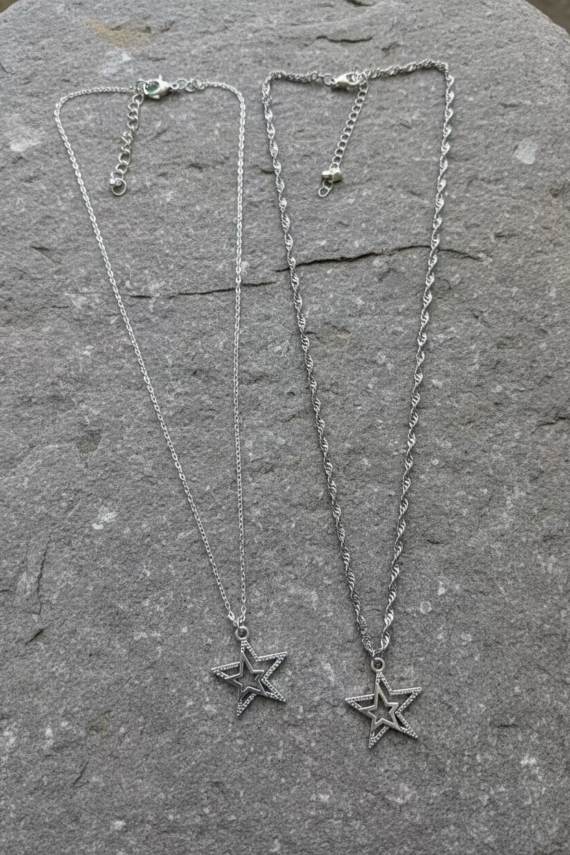Two silver star pendant necklaces with chain clasp closures, displayed on a textured gray stone surface.