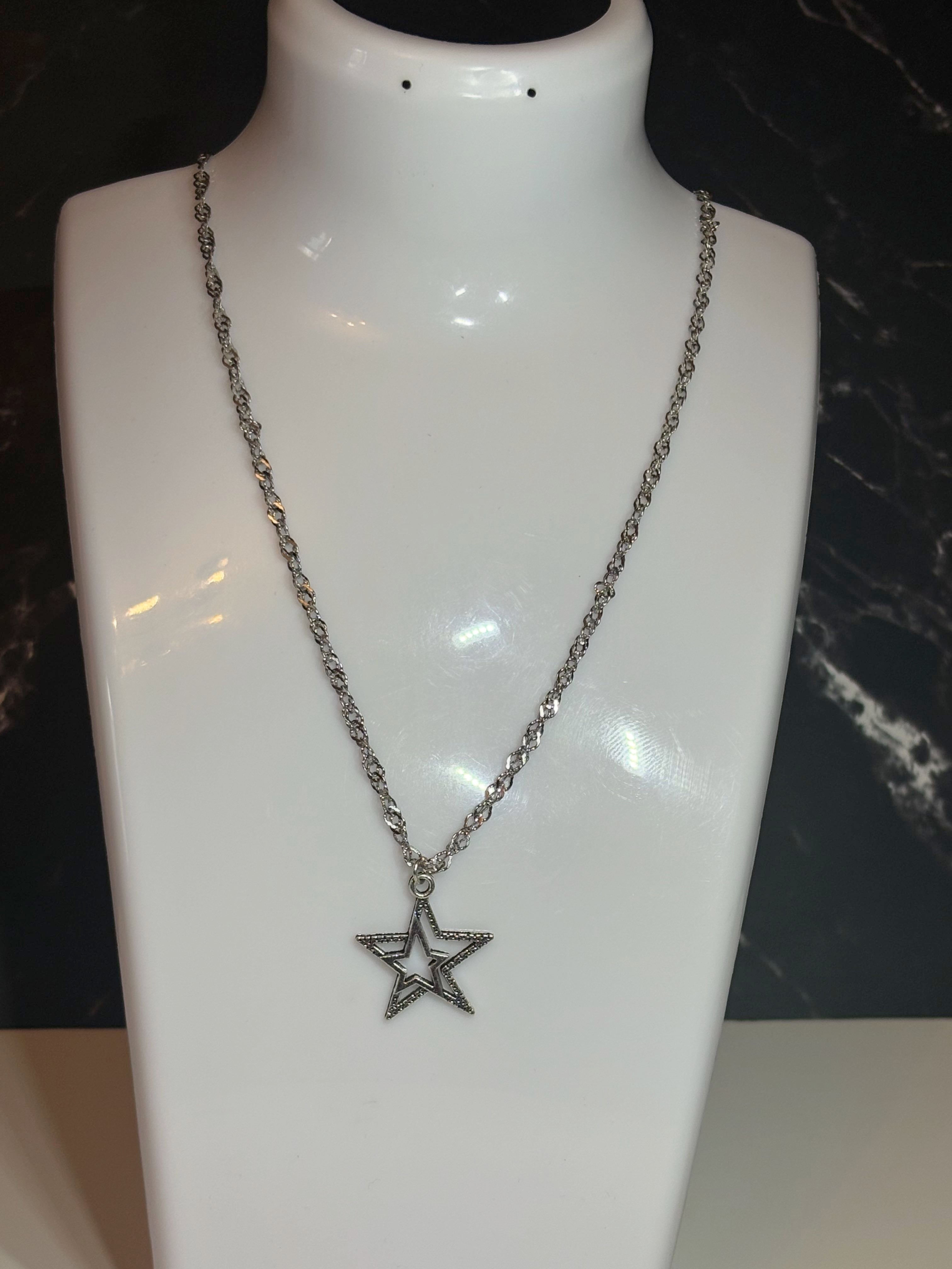 A silver-toned chain necklace with a star-shaped pendant, displayed on a glossy white mannequin bust against a dark background.