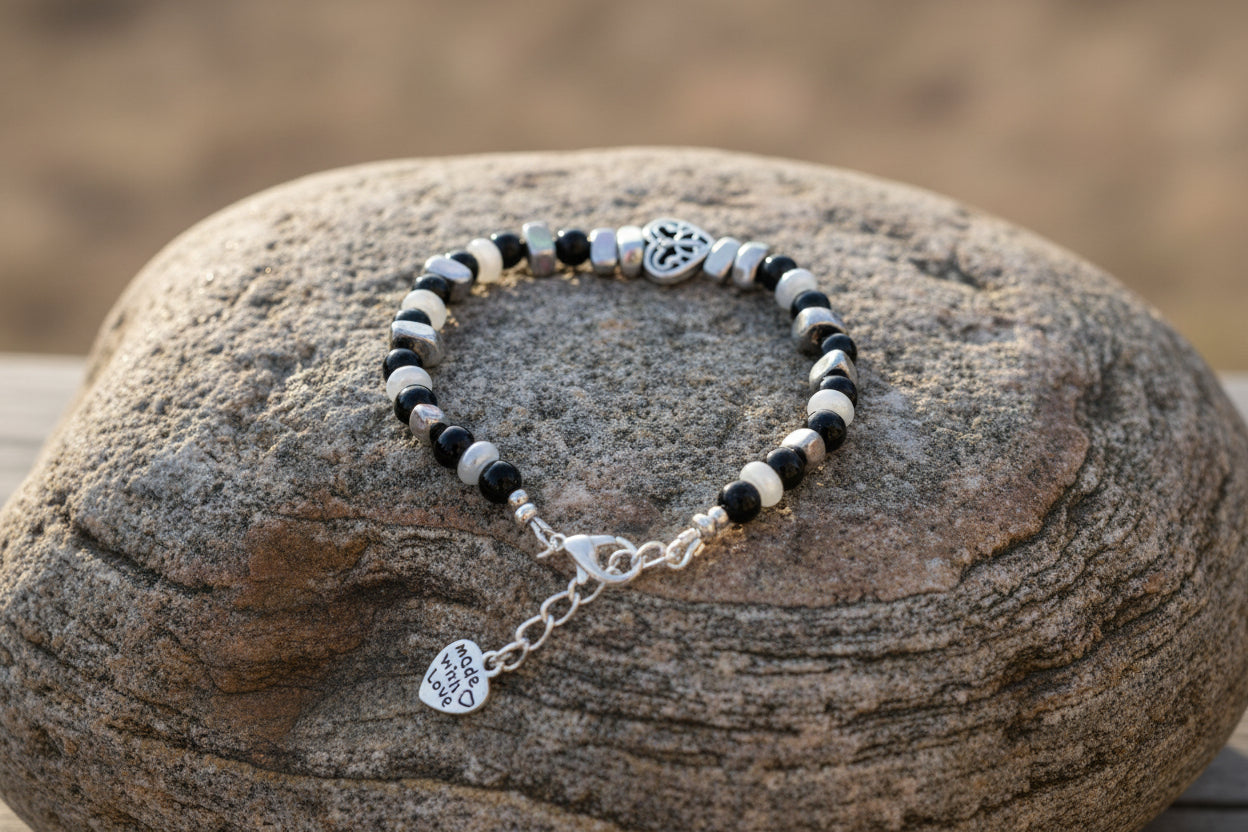 A beaded bracelet with alternating black and silver-gray metal beads, featuring a silver heart-shaped charm and a small dangling heart charm on a large brown stone.