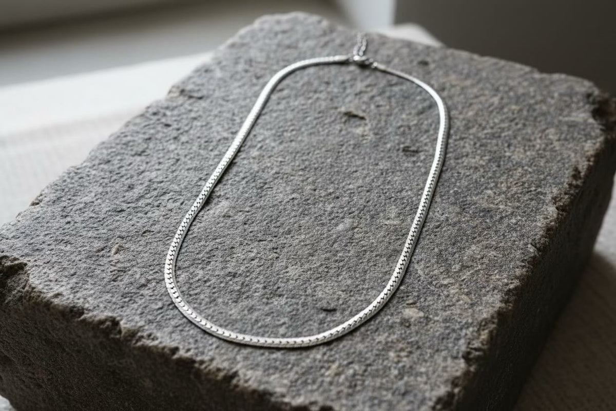 A silver snake chain necklace draped over a textured dark gray stone block.