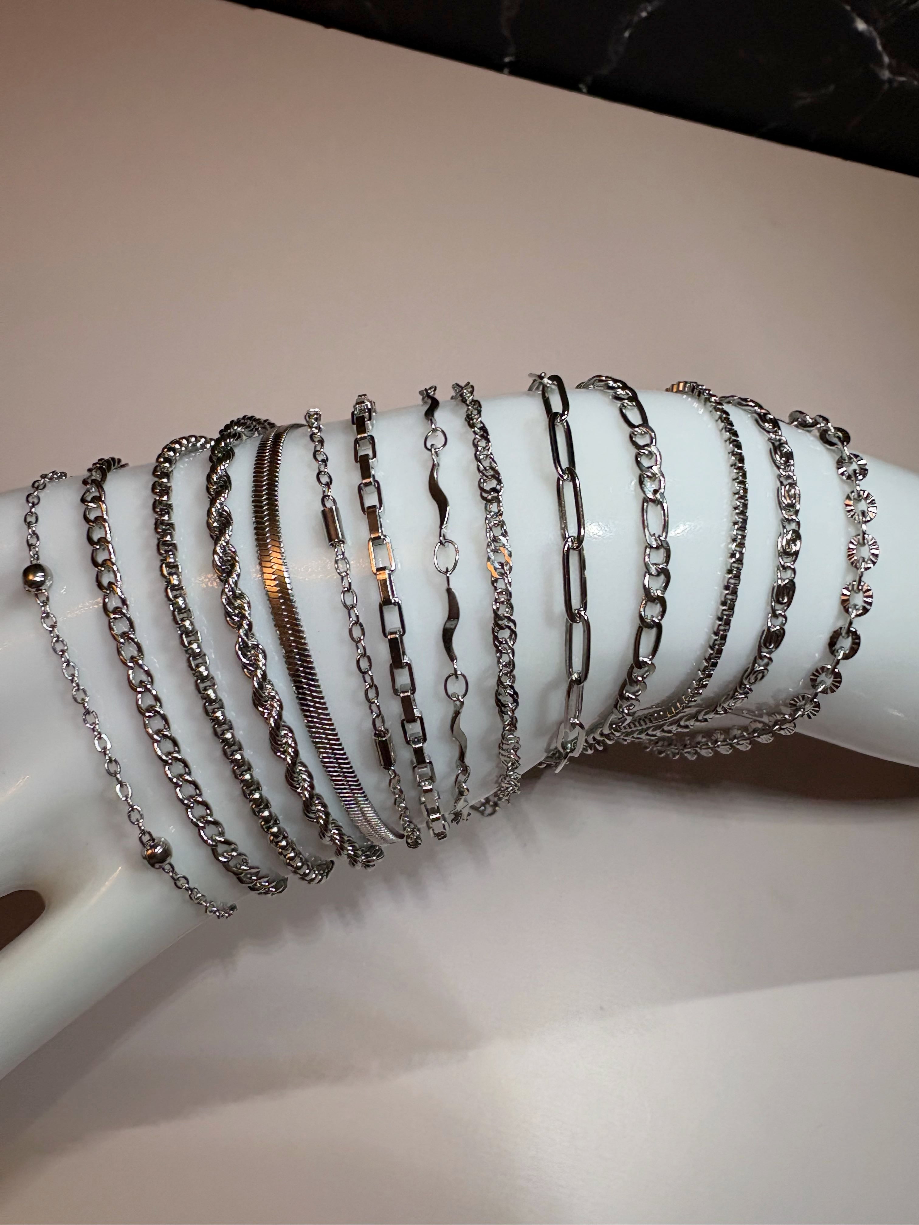 A group of multiple silver-toned chain bracelets displayed on a white mannequin arm against a light beige background.