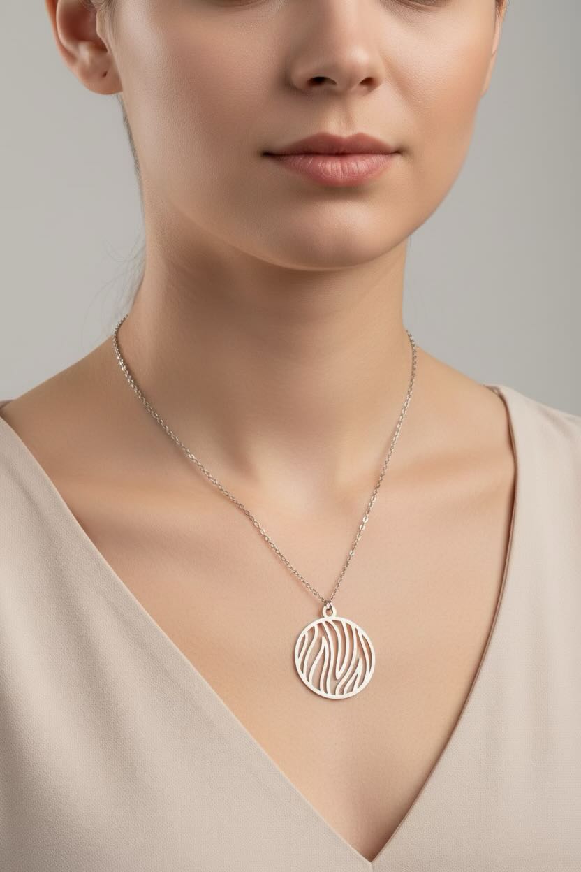 A close-up of a woman wearing a delicate silver necklace with a circular pendant featuring a flame cutout pattern, paired with a beige V-neck top against a neutral gray background.